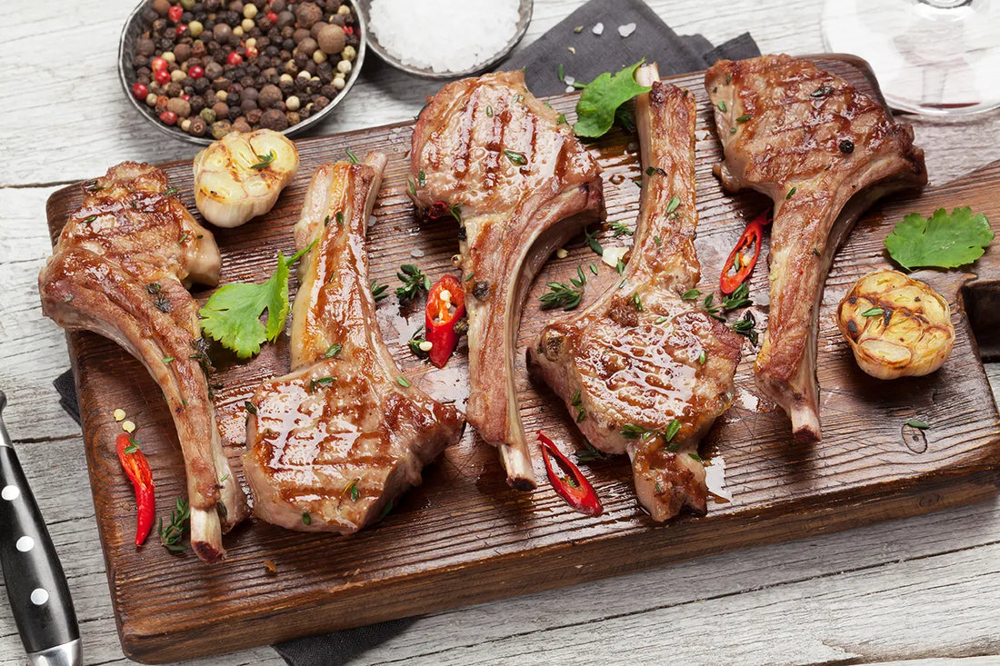 A close-up of tender, succulent lamb chops sizzling on a wooden chopping board, cooked to perfection on the BBQ. The golden brown exterior gives way to a juicy pink interior, making these lamb chops a delicious and satisfying meal.