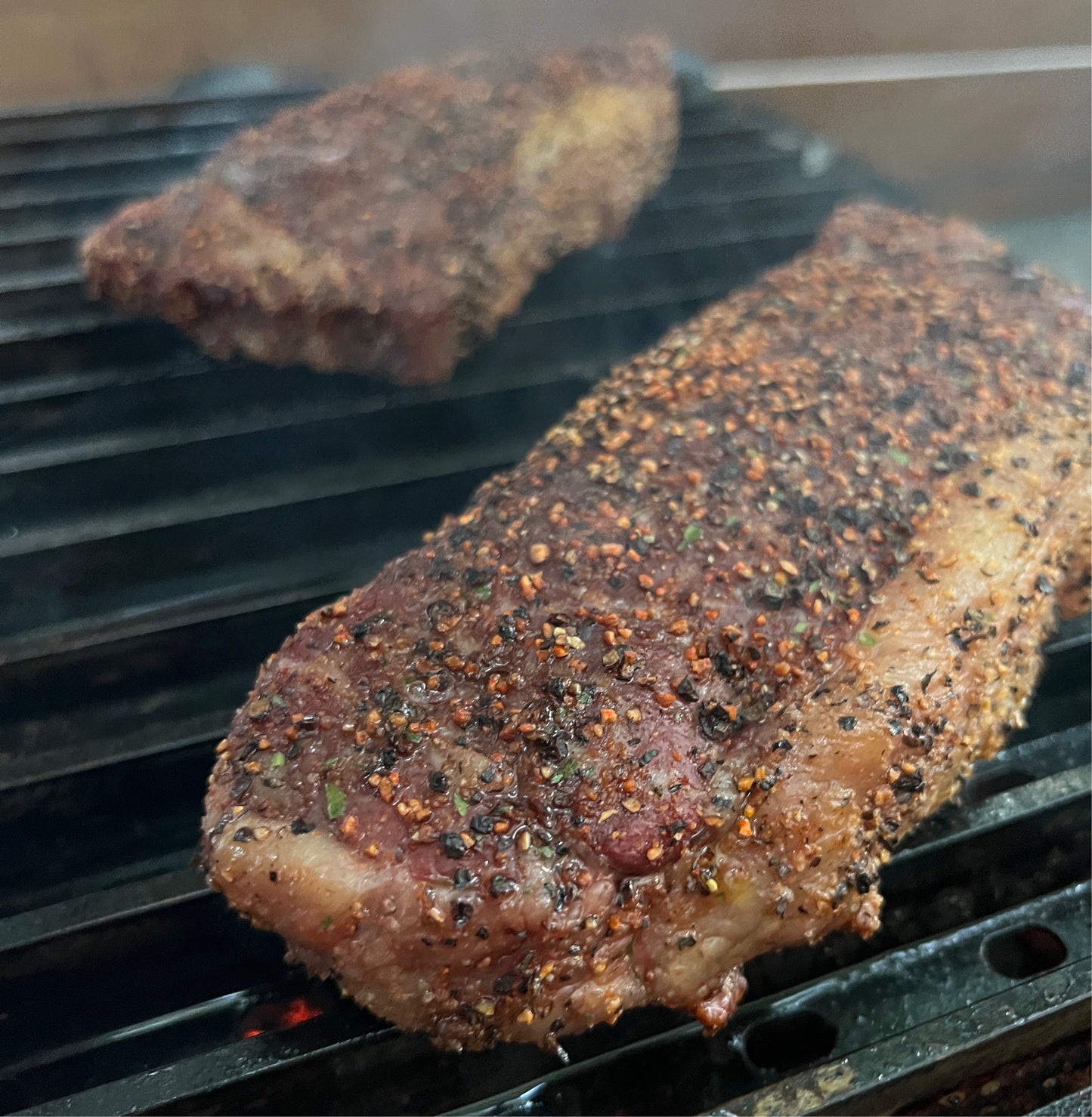 Two juicy steaks seasoned with Meat Church Holy Cow rub, sizzling on a grill grate for a Weber gas BBQ, ready to be cooked to perfection